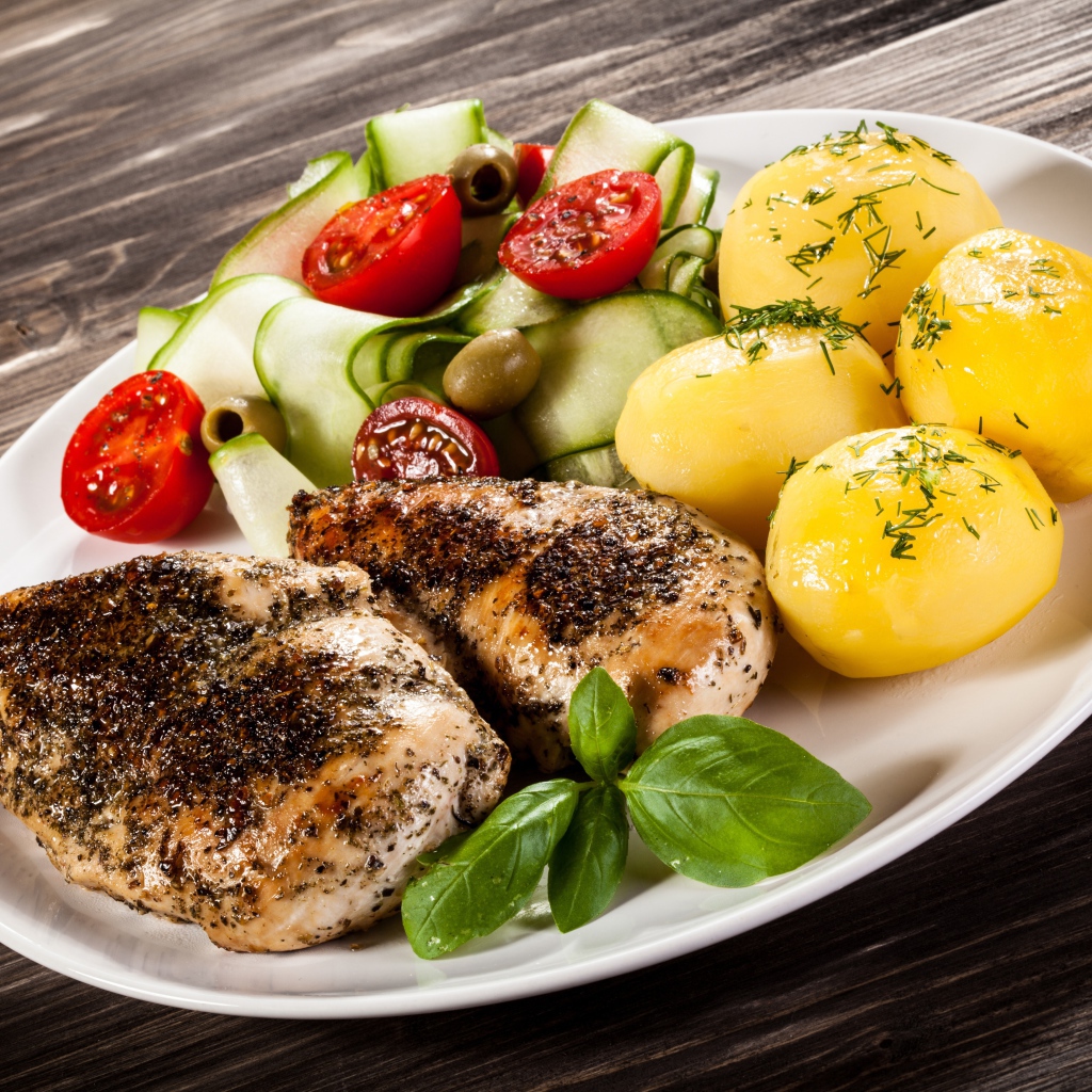 Куски курицы на тарелке с картофелем, помидорами и кабачком 