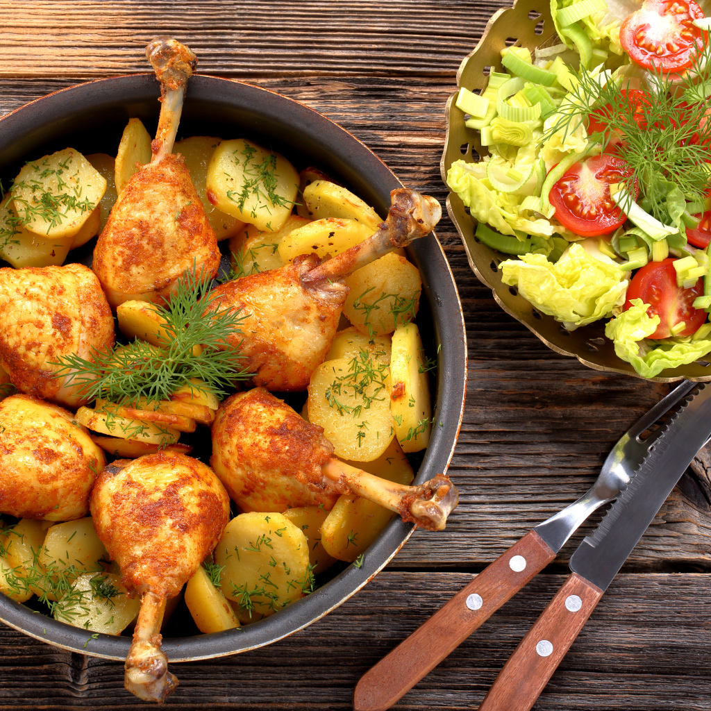 Fried chicken legs with potatoes on a table with salad