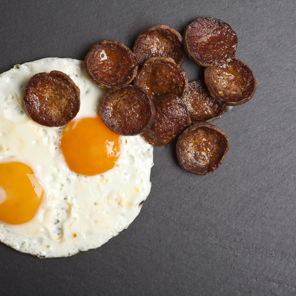 Жареная колбаса с яичницей глазуньей на сером столе 