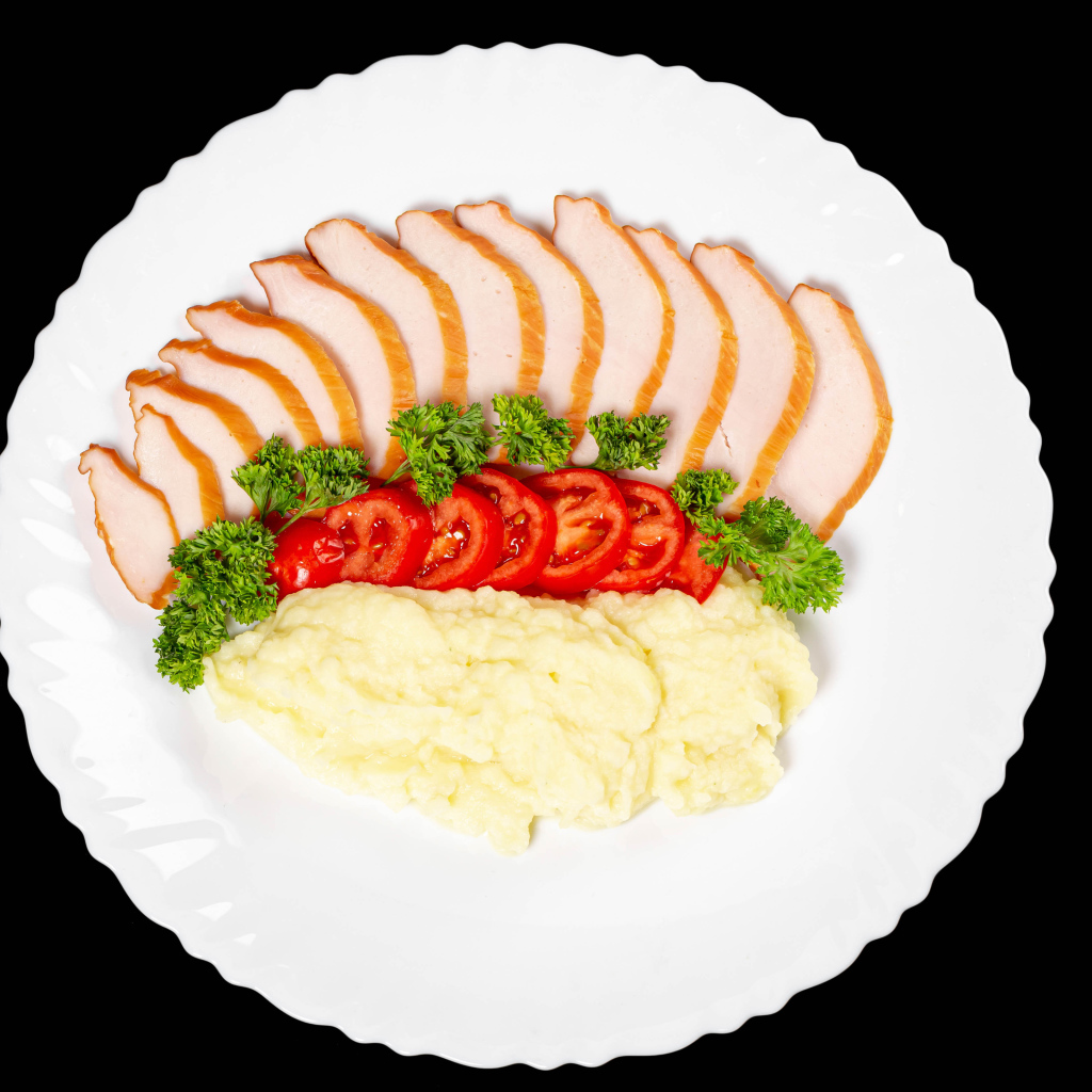 Ham on a large white plate with potatoes and tomatoes