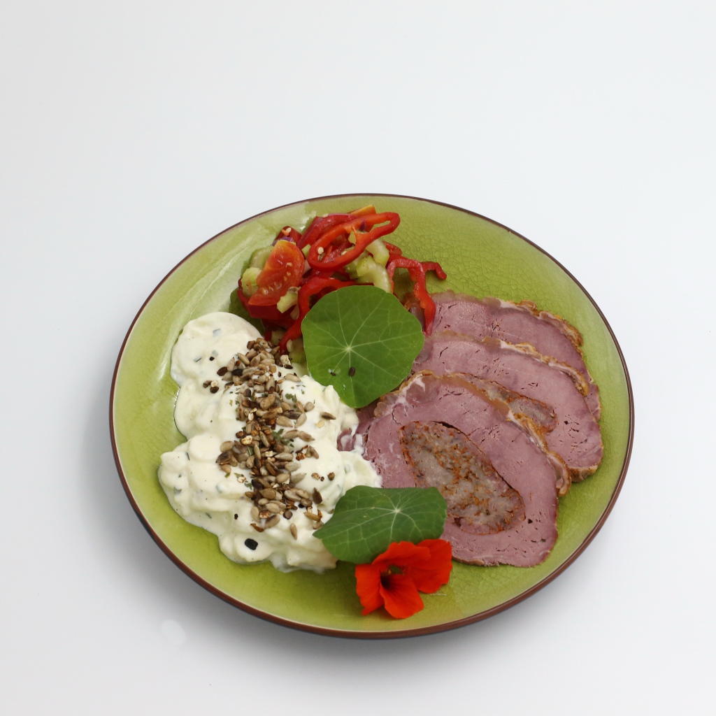 Мясо с соусом и овощами на тарелке на сером фоне