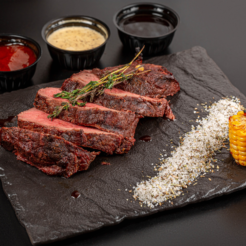 Кусок запеченного мяса на доске с кукурузой и специями 