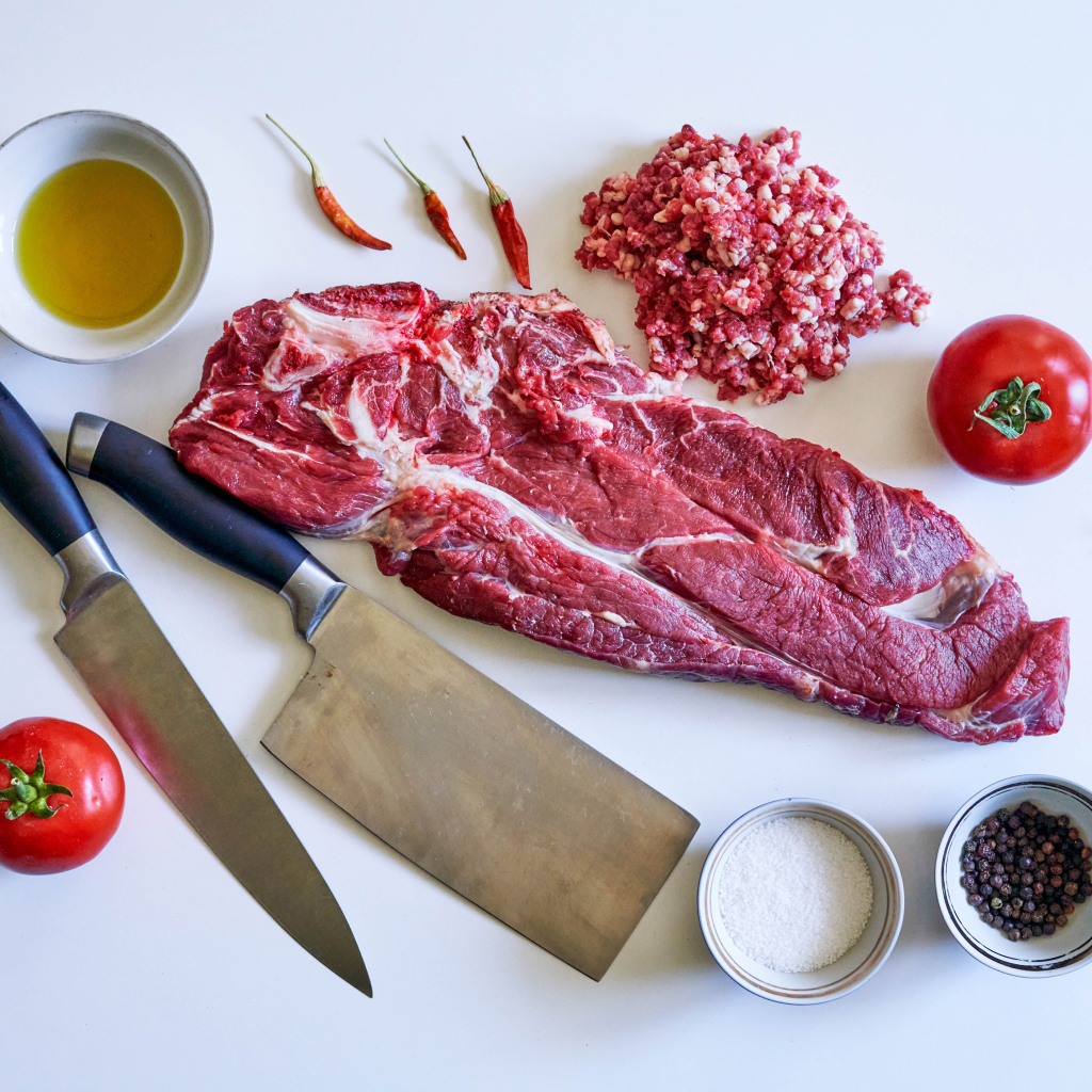 Кусок мяса со специями и ножами на столе 