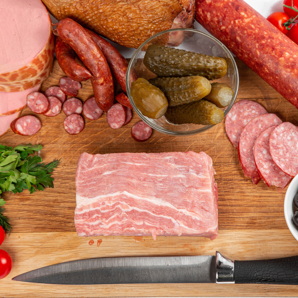 Колбаса на столе с огурцами, помидорами и зеленью 