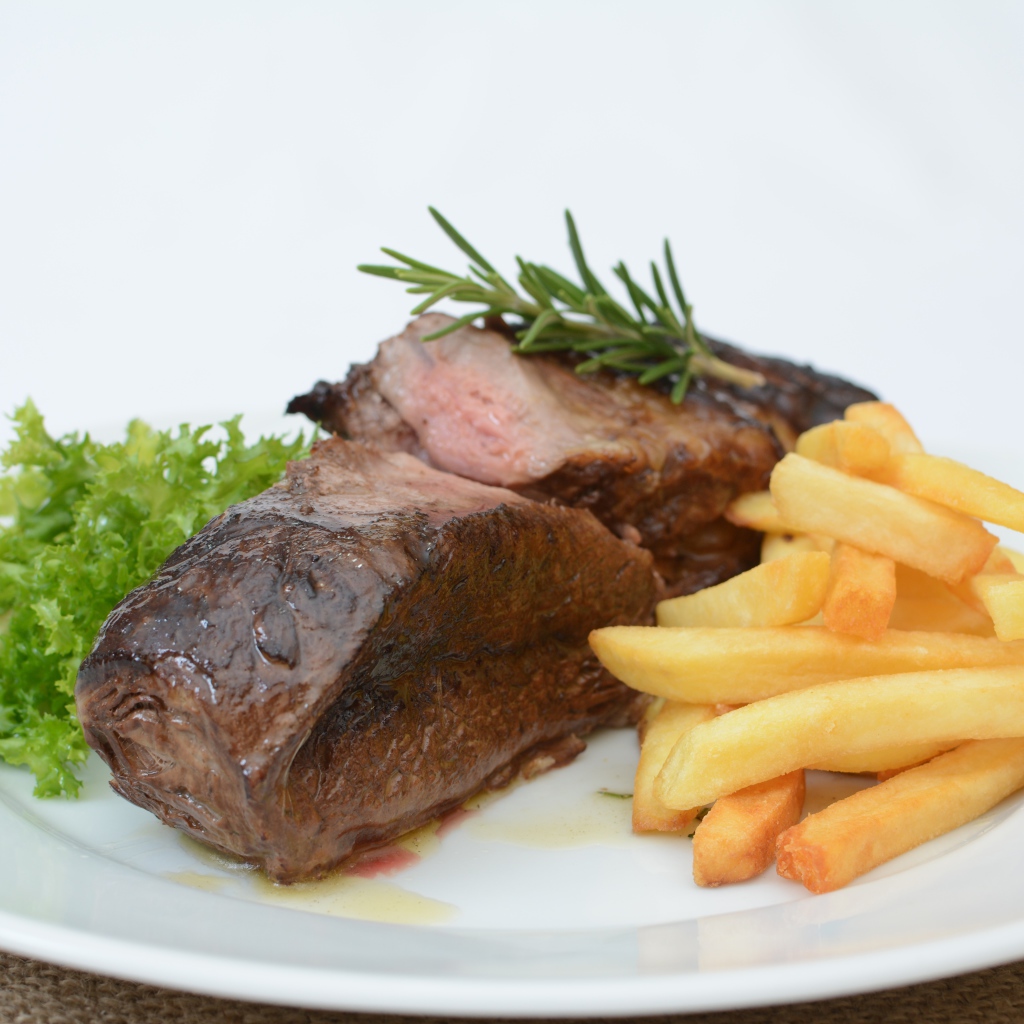 Два куска мяса на тарелке с картофелем фри 