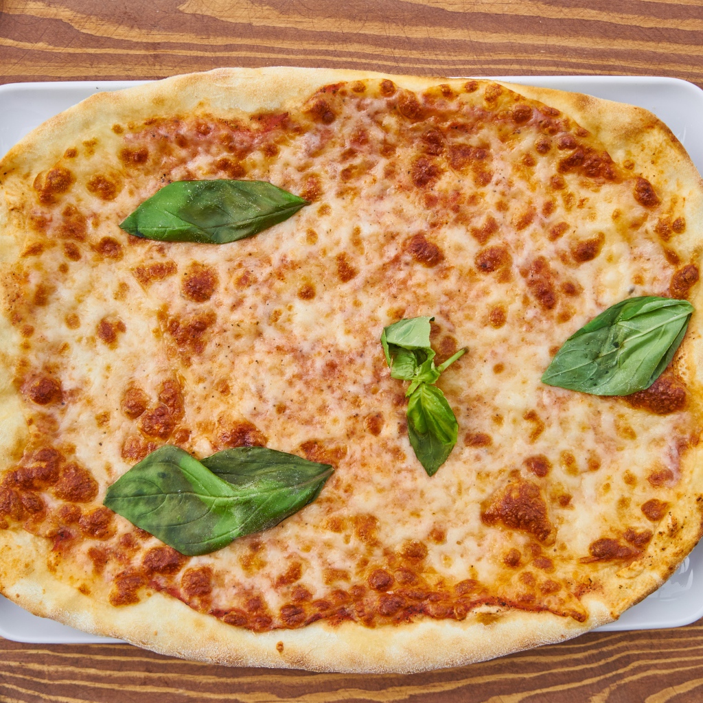 Пицца с сыром и листьями базилика на столе со столовыми приборами