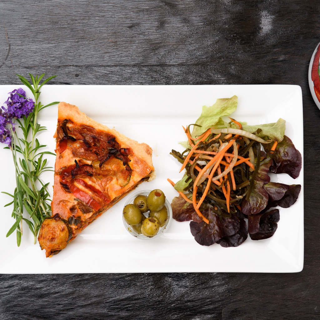 Кусок пиццы с салатом и оливками на белой тарелке