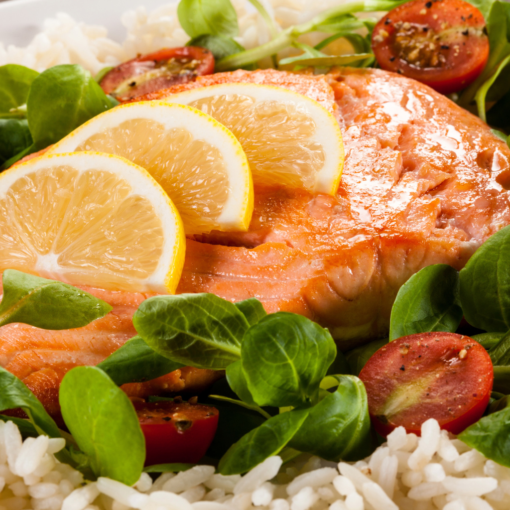 Кусок запеченной красной рыбы на тарелке с лимоном, рисом, базиликом и помидорами