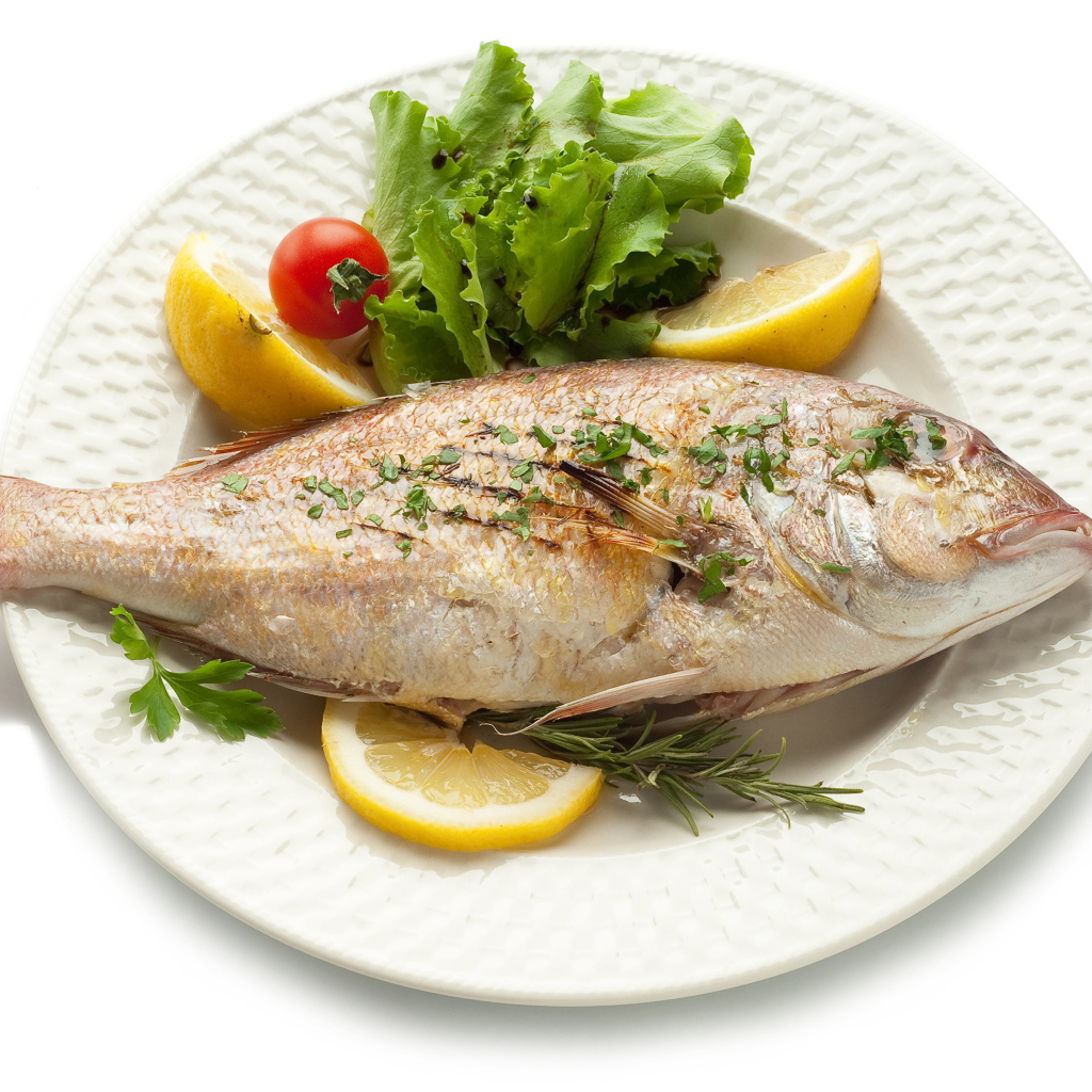 Запеченная рыба на тарелке с зеленью и лимоном