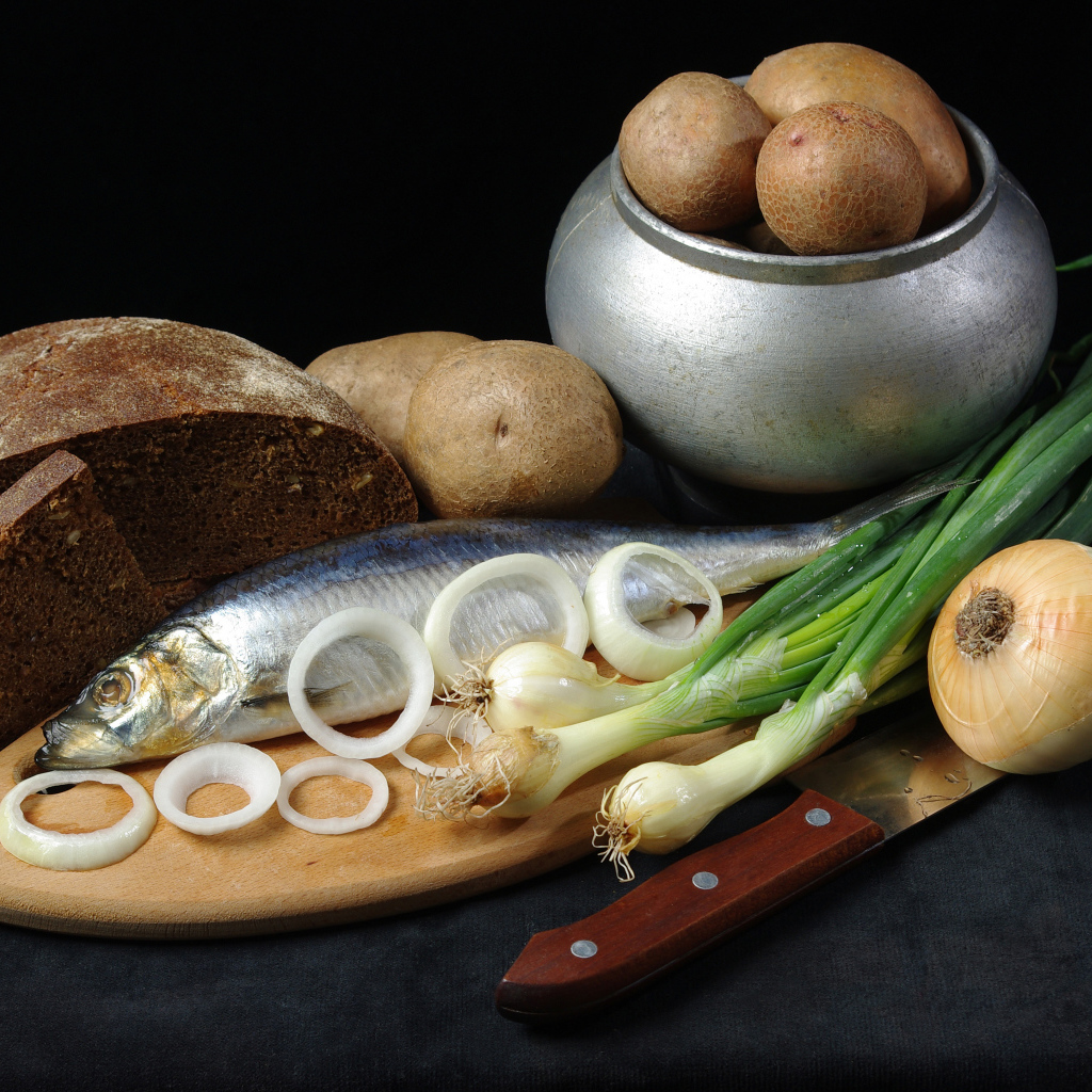 Сельдь на столе с картофелем, черным хлебом и луком 