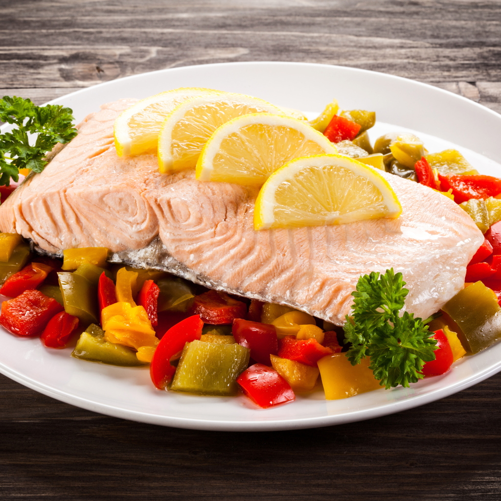 Кусок рыбы на тарелке с овощами и лимоном