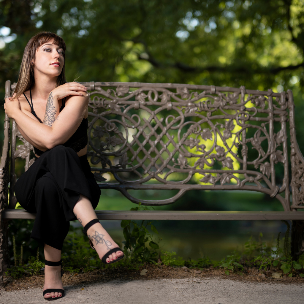 Девушка в черном костюме сидит на лавке 