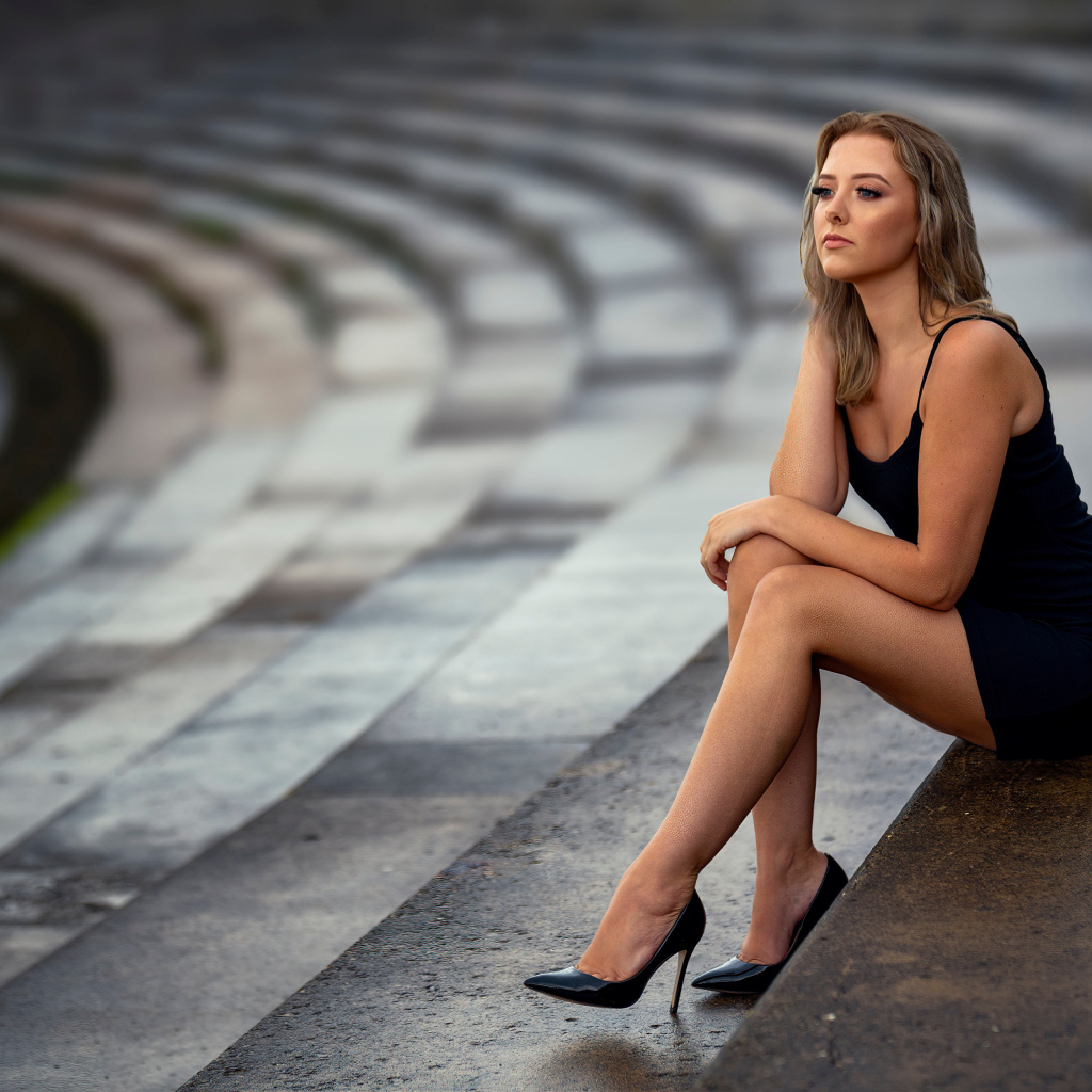 Девушка в коротком черном платье сидит на ступеньках