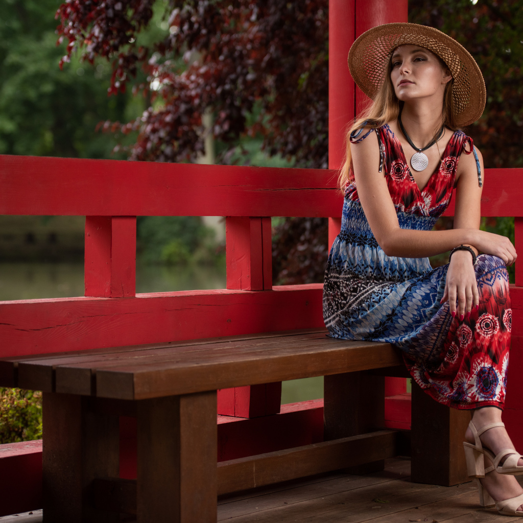 Молодая девушка в платье сидит на лавке 