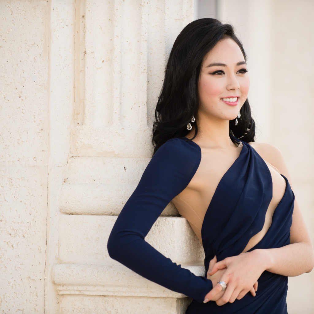 Молодая девушка в платье стоит у стены 