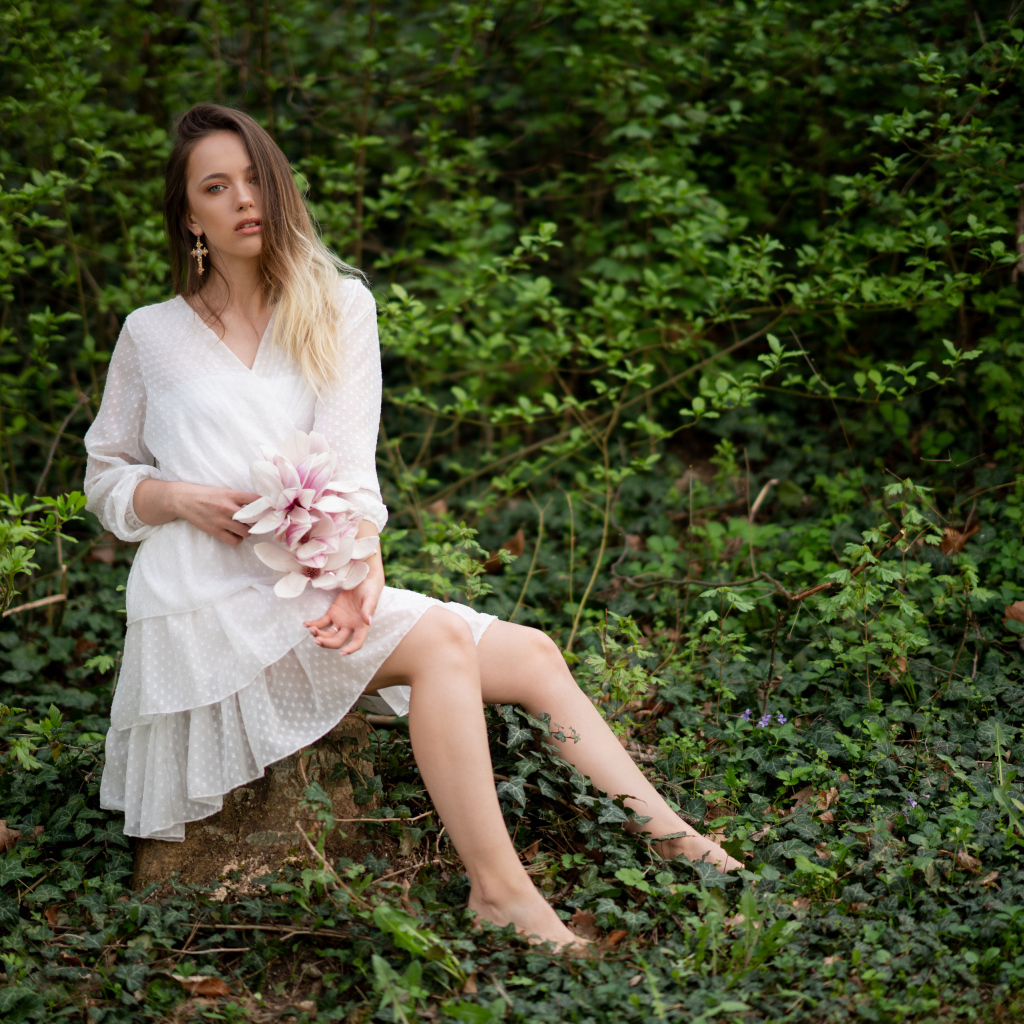 Молодая девушка в белом платье сидит на камне в лесу 