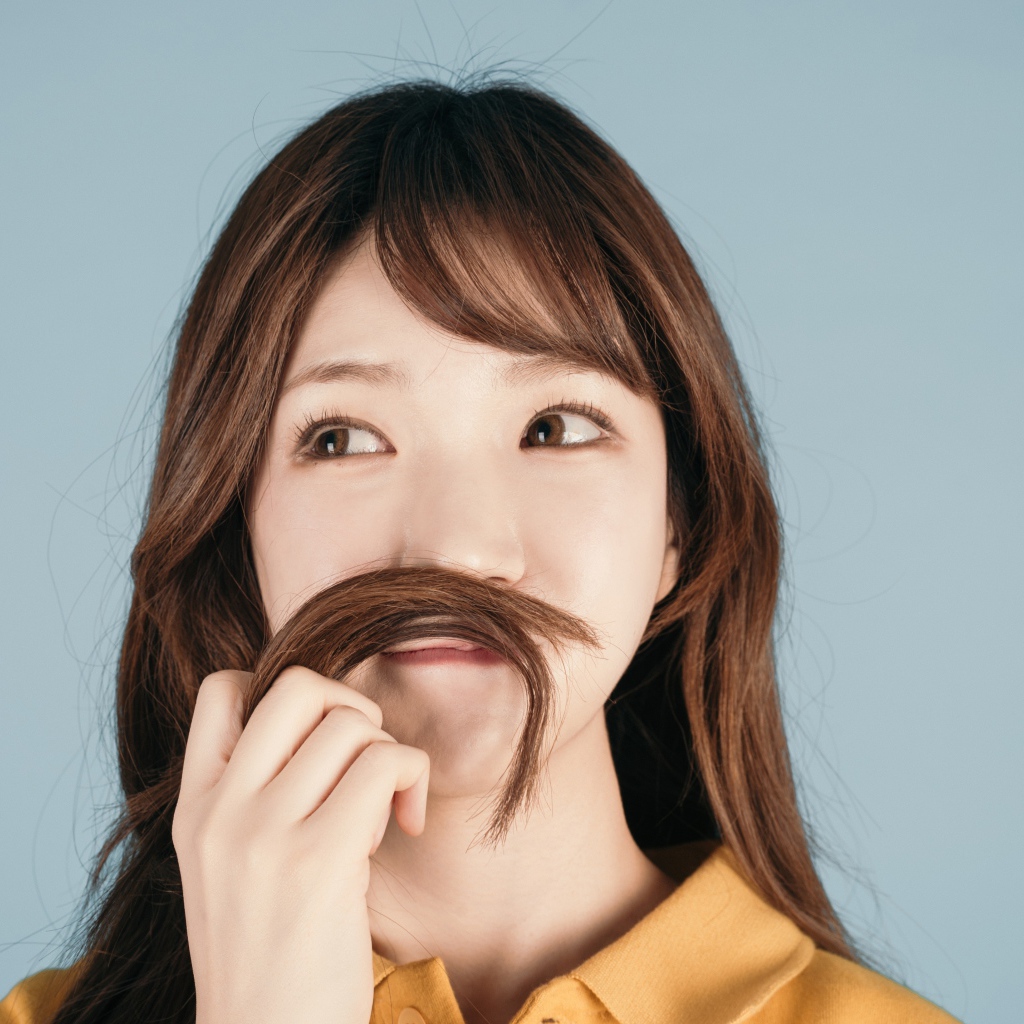 Девушка азиатка закрыла лицо волосами на сером фоне 