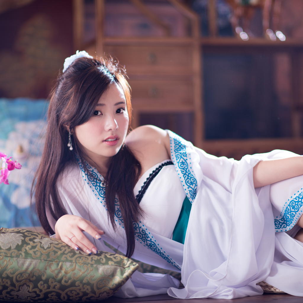 Девушка азиатка в красивом платье лежит на кровати 