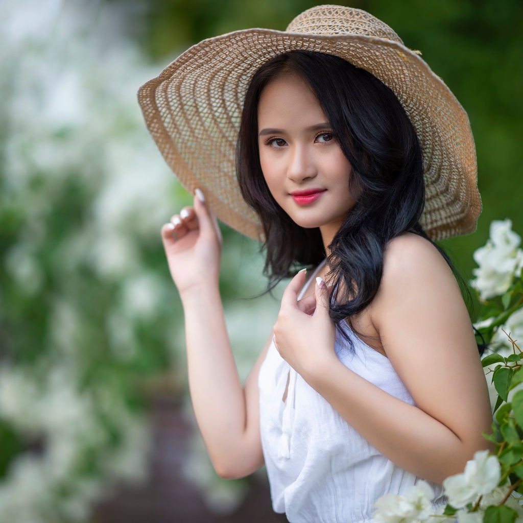 Девушка азиатка в большой шляпе у зеленого куста