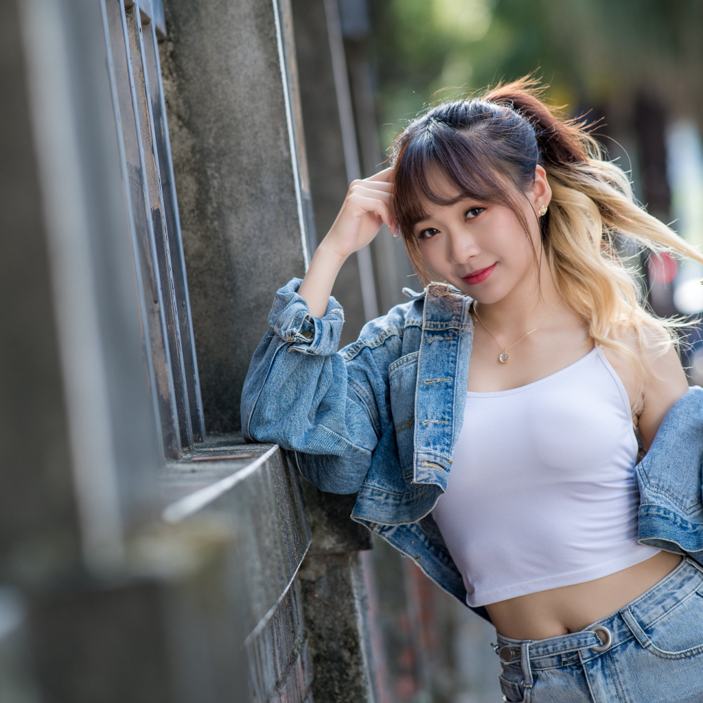 Девушка азиатка в джинсовой куртке у забора 