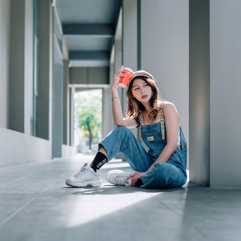 Девушка азиатка в синем комбинезоне с кофе в руке 