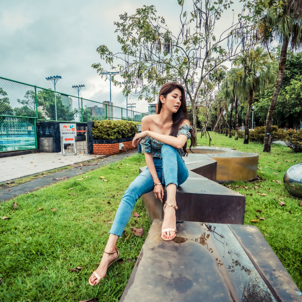 Девушка азиатка в джинсах сидит в парке 