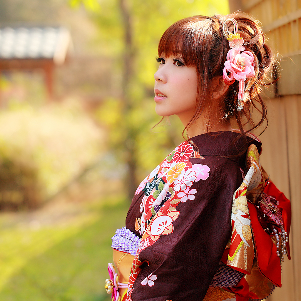 Девушка азиатка в кимоно стоит у забора 