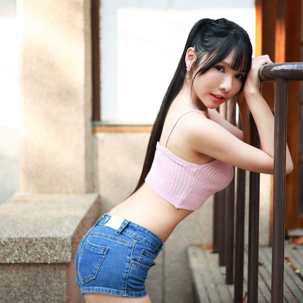 Девушка азиатка в коротких шортах стоит у перил 