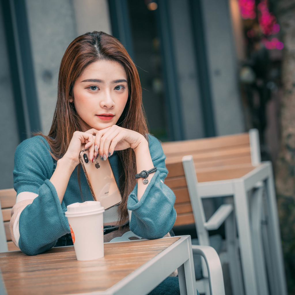 Девушка азиатка сидит за столом в кафе с телефоном 