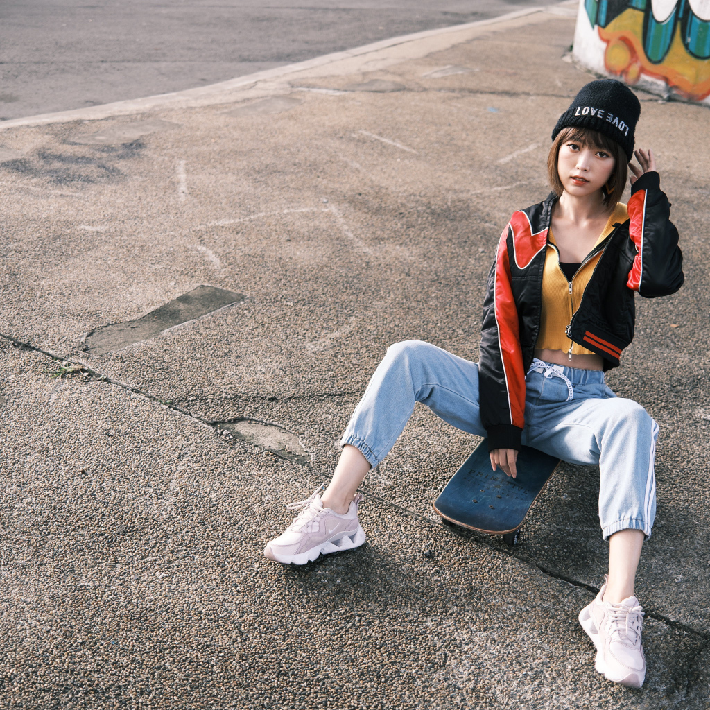 Девушка азиатка сидит на скейтборде на асфальте 