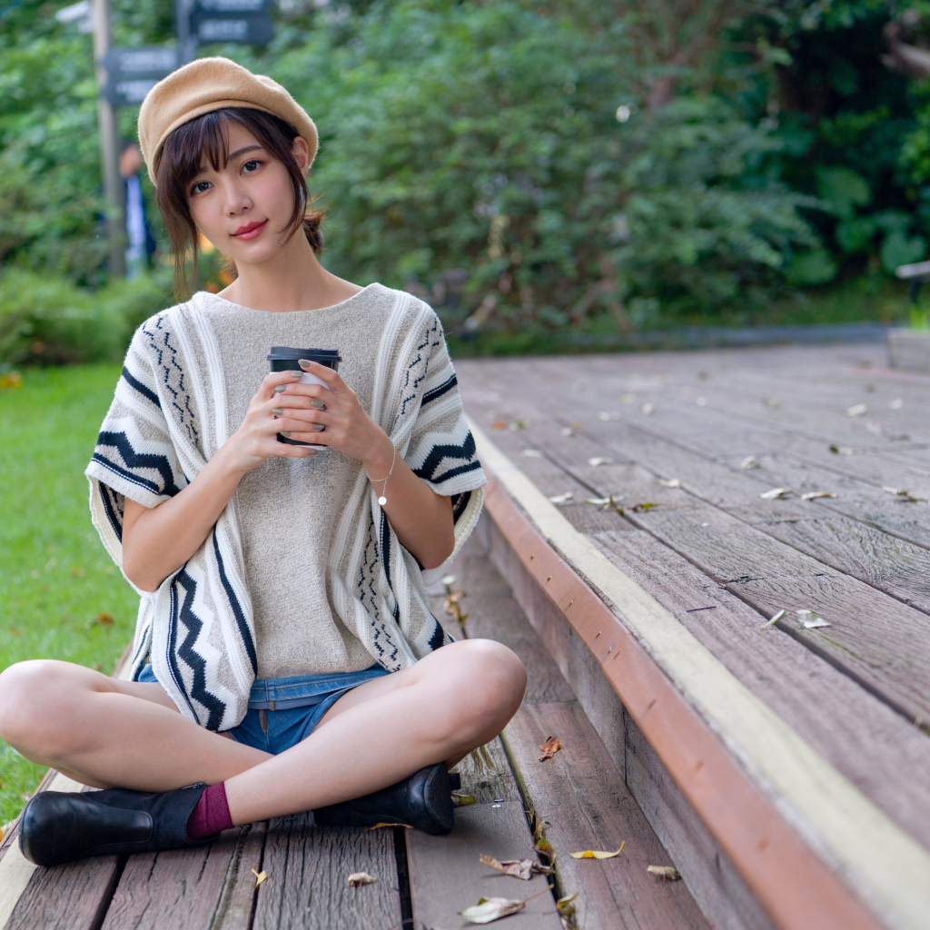 Девушка азиатка сидит с кофе в осеннем парке 