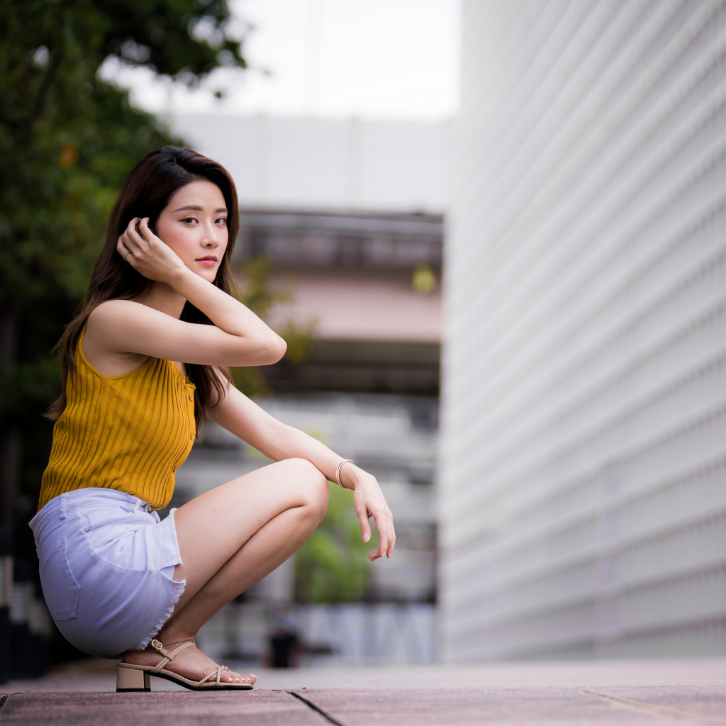 Девушка азиатка сидит на корточках у стены