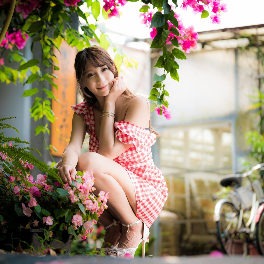 Девушка азиатка сидит на корточках у розового цветка