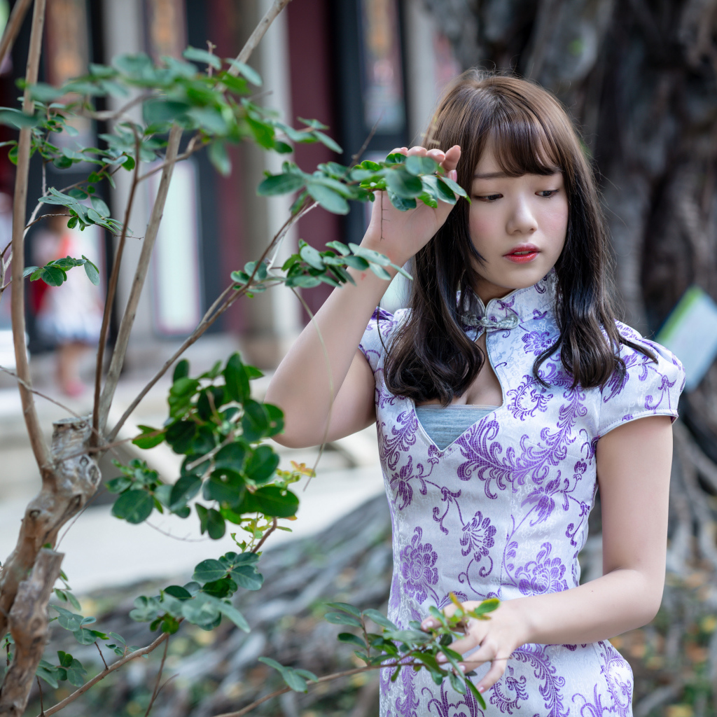 Красивая девушка азиатка в платье стоит у дерева 