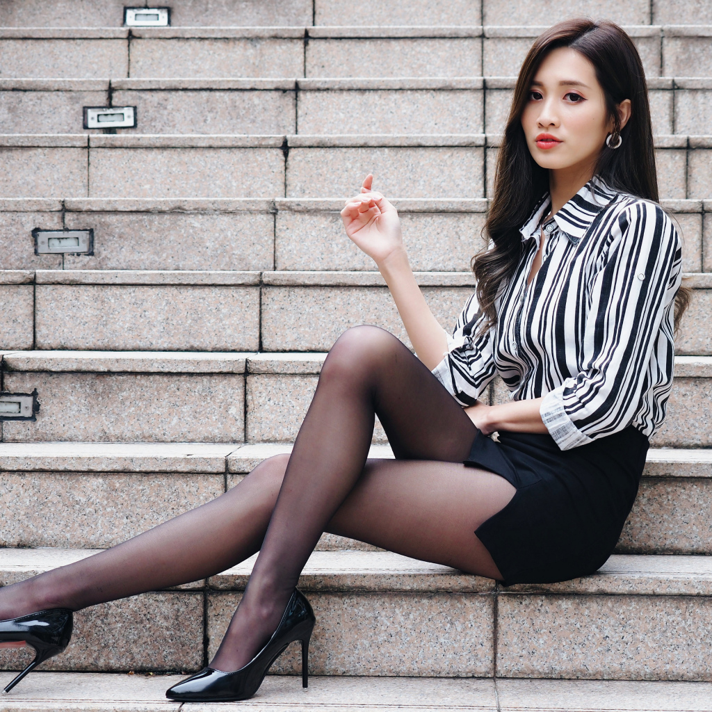 Красивая девушка азиатка в юбке сидит на ступеньках