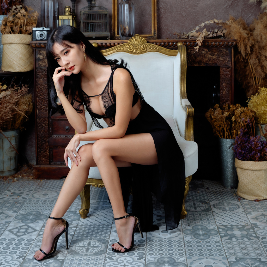 Красивая девушка азиатка в черном платье сидит в белом кресле 