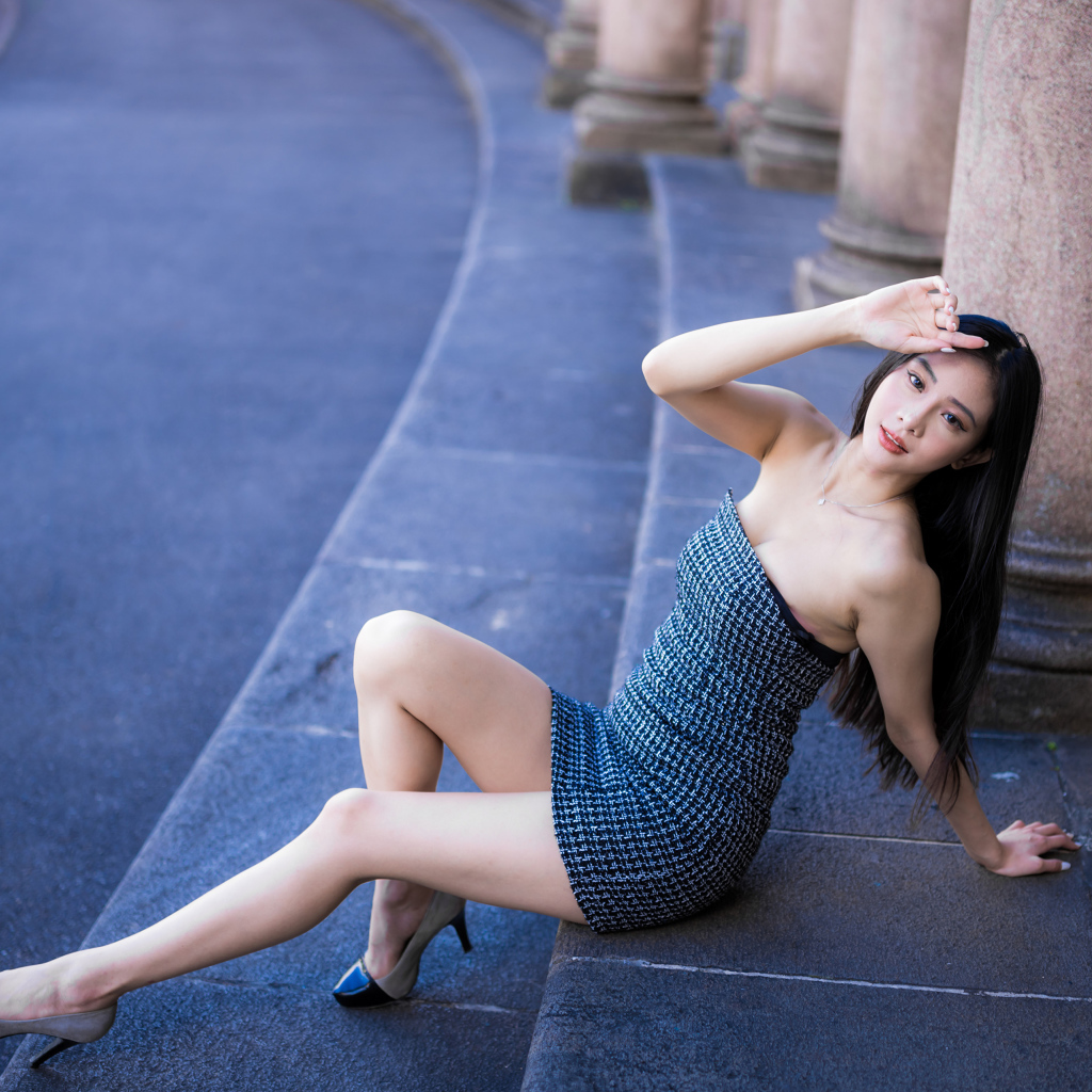 Красивая девушка азиатка в сером платье сидит на ступеньках