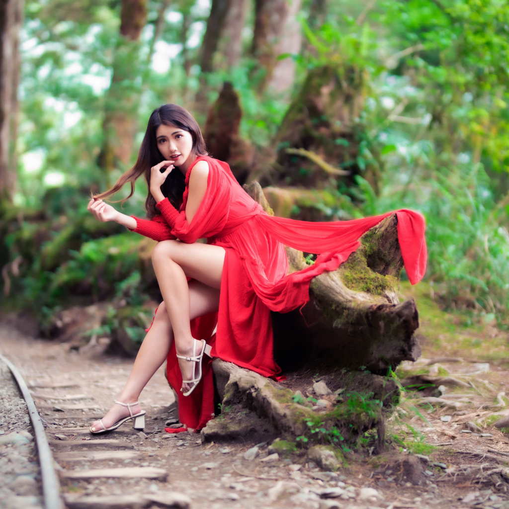 Красивая азиатка в красном платье сидит на дереве 