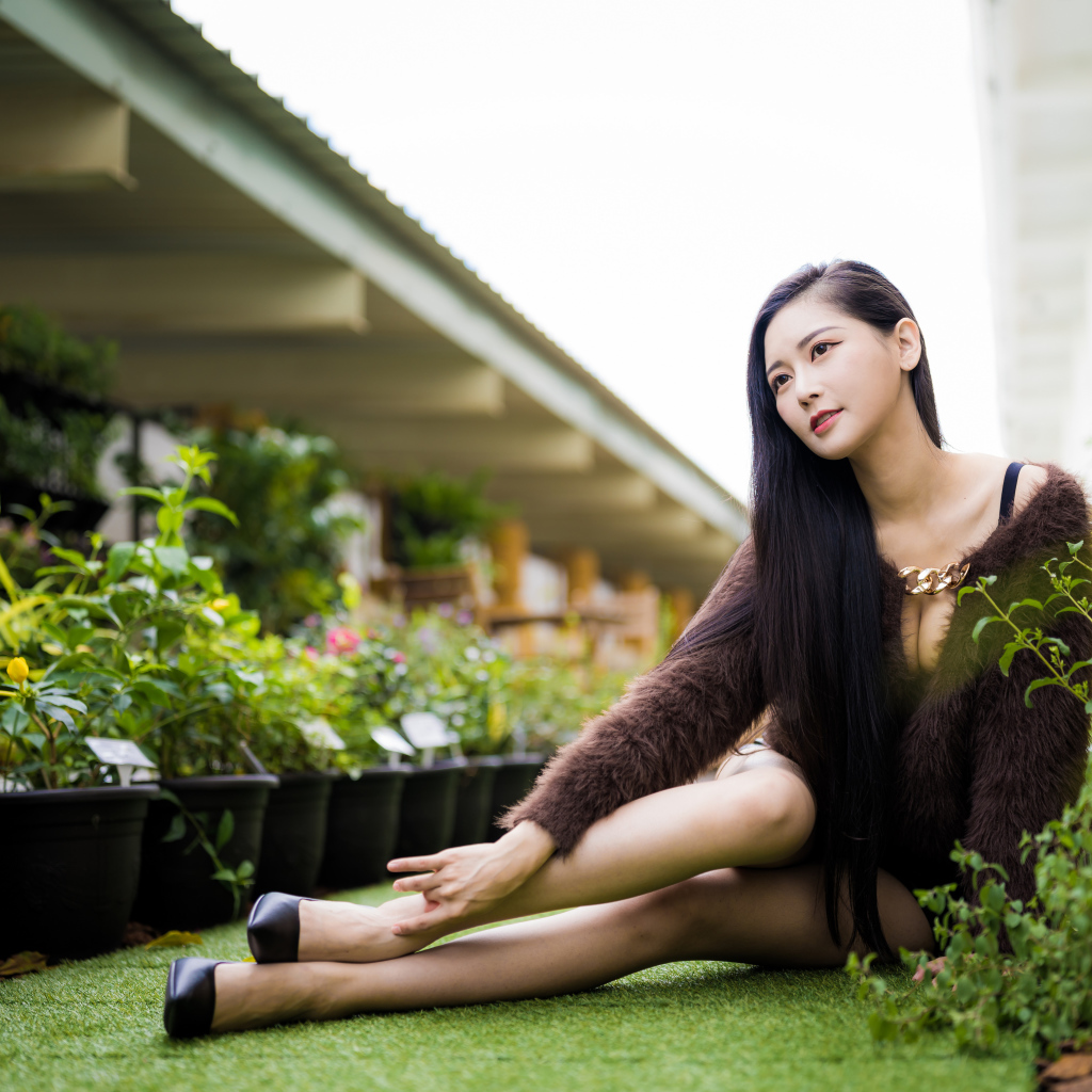 Красивая азиатка сидит на земле у цветов