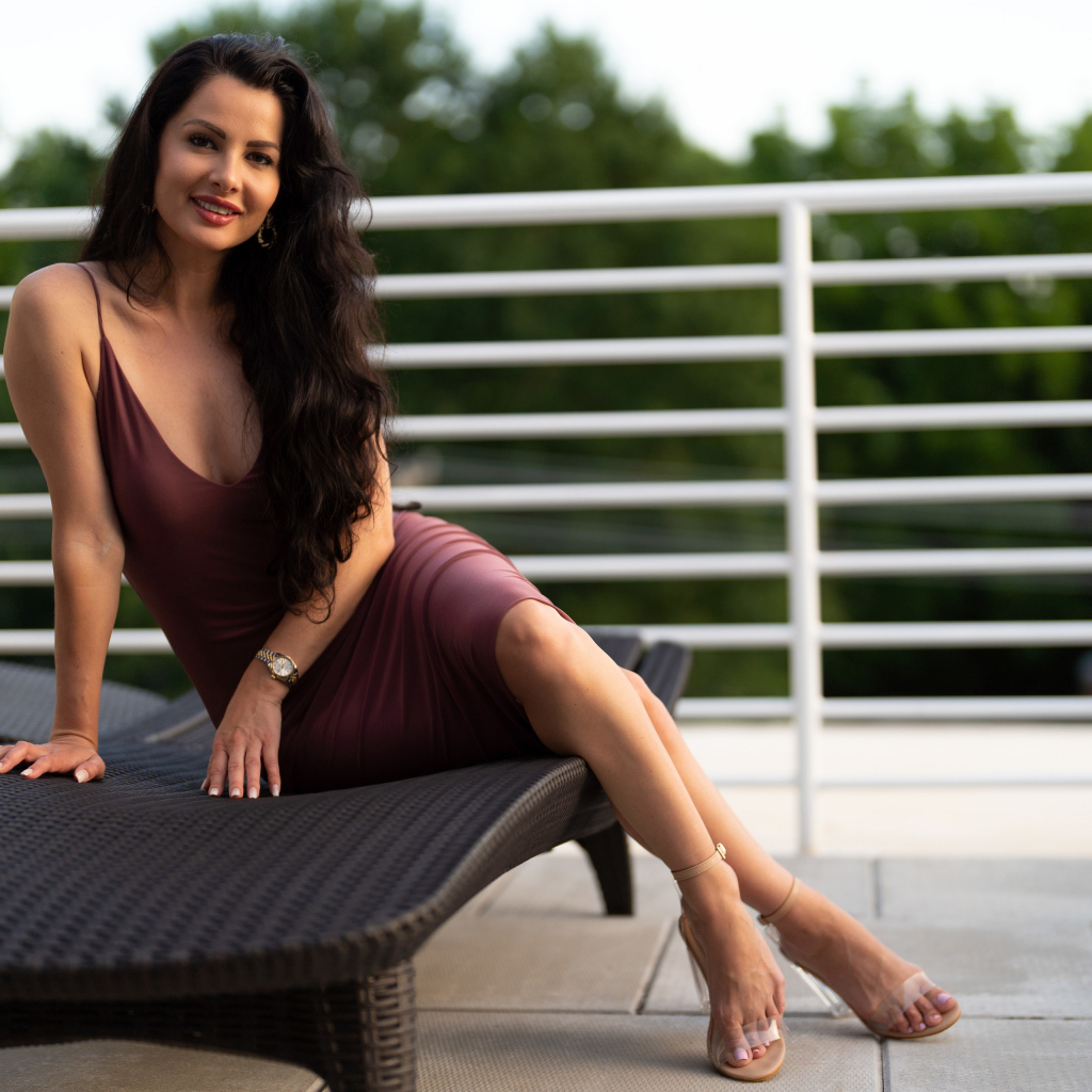 Красивая брюнетка в платье сидит на диване 