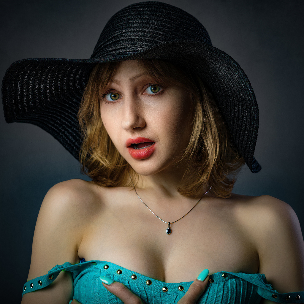 Красивая девушка в большой черной шляпе на сером фоне 