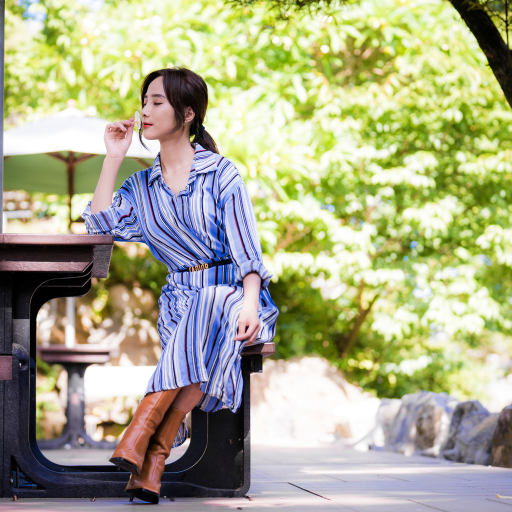 Красивая девушка в платье сидит за столиком в парке