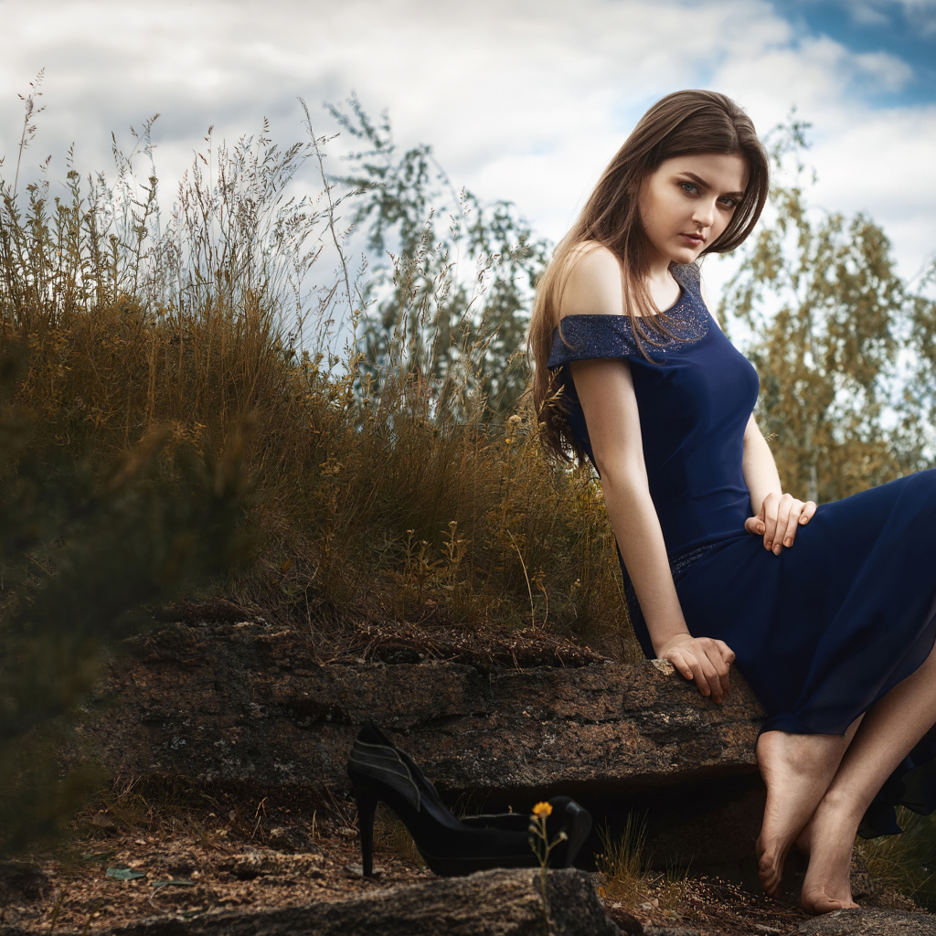 Красивая девушка в длинном синем платье сидит на камне 