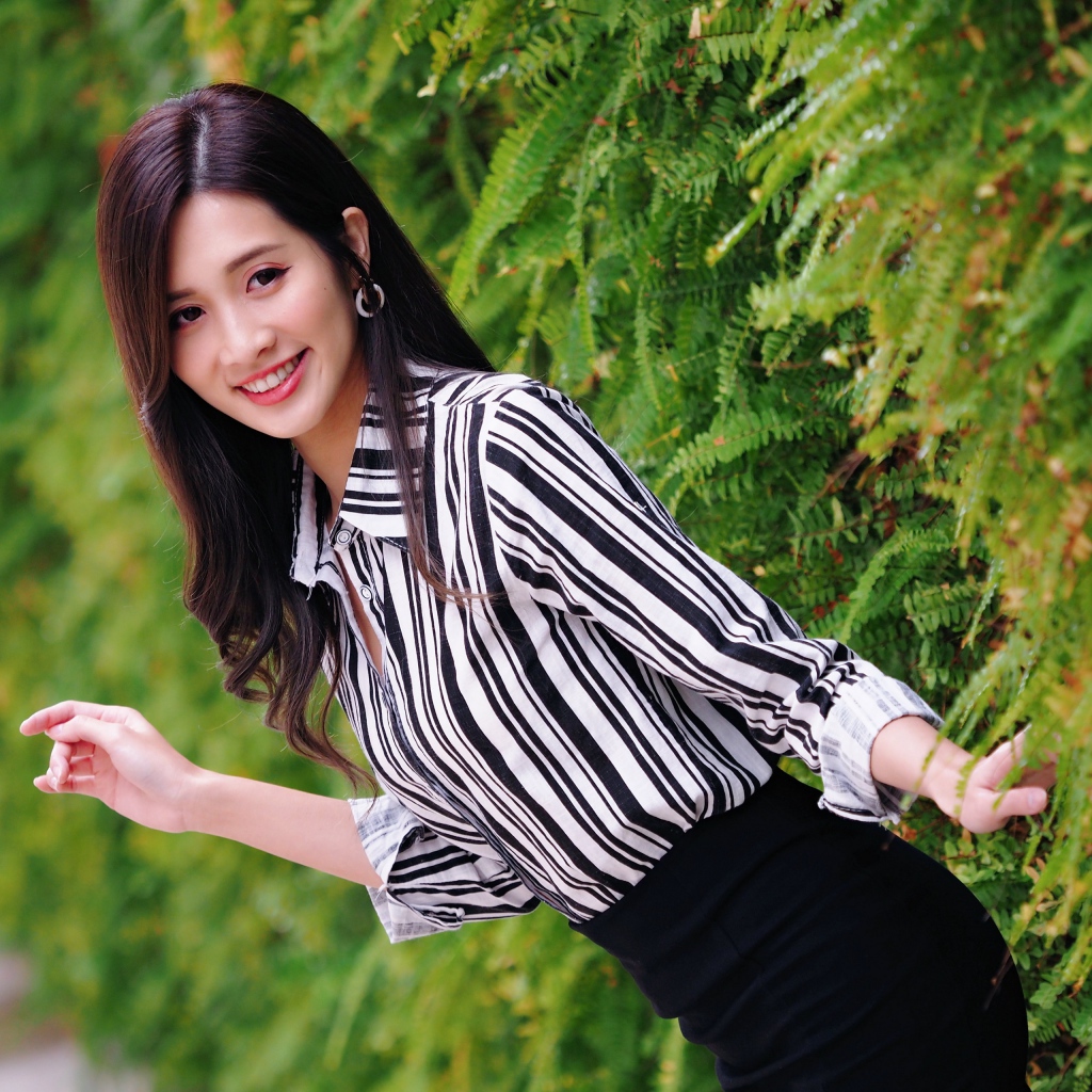 Красивая девушка в полосатой рубашке стоит у растения