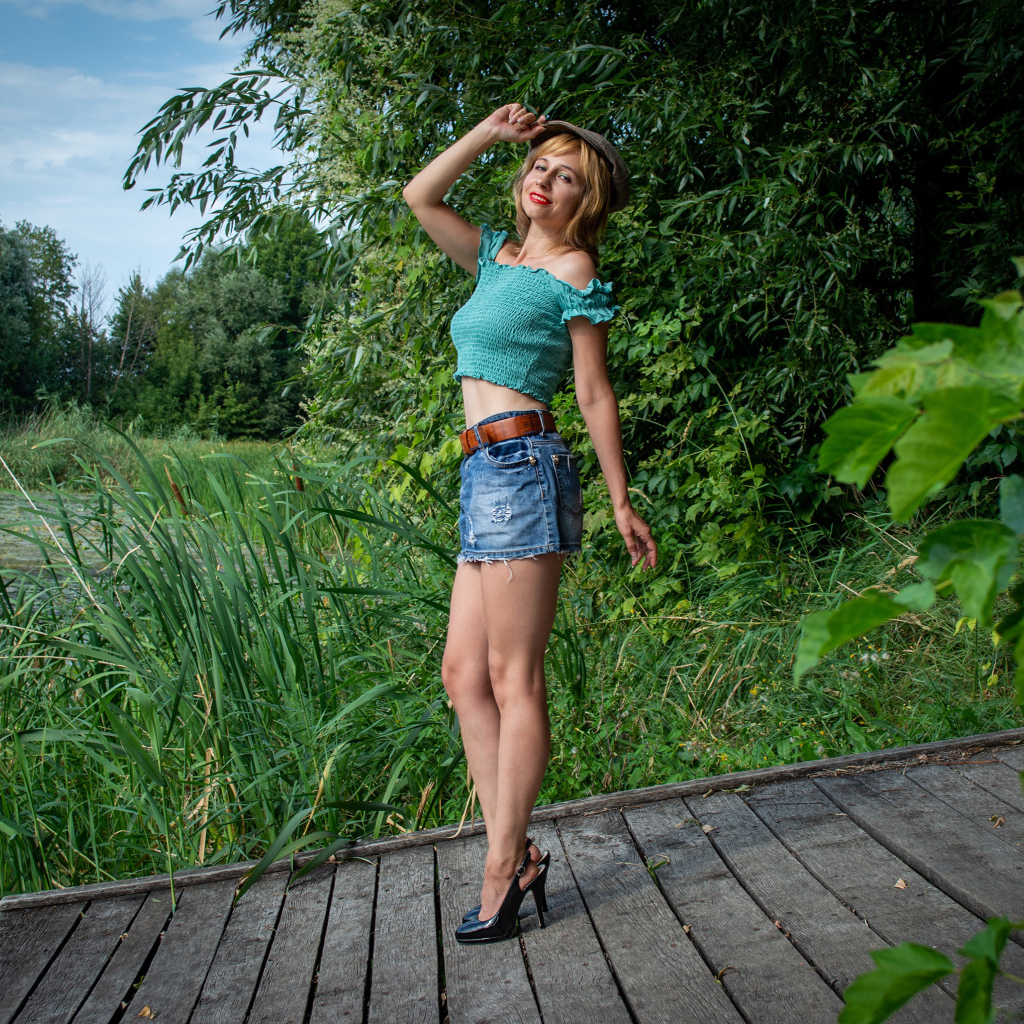 Красивая девушка в джинсовой юбке у пруда 