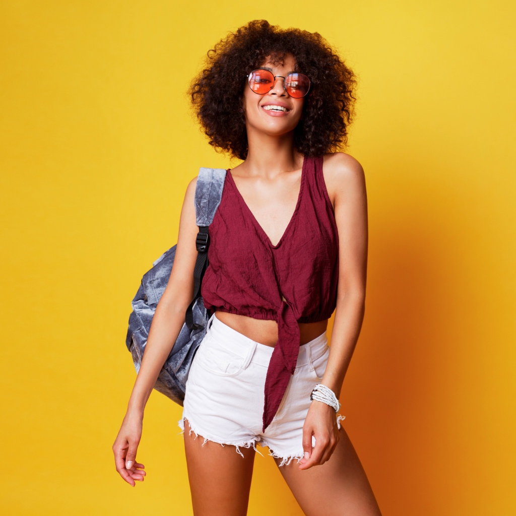 Красивая девушка в очках с рюкзаком на желтом фоне 