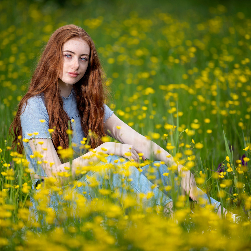 Голубоглазая девушка сидит на поле с желтыми цветами