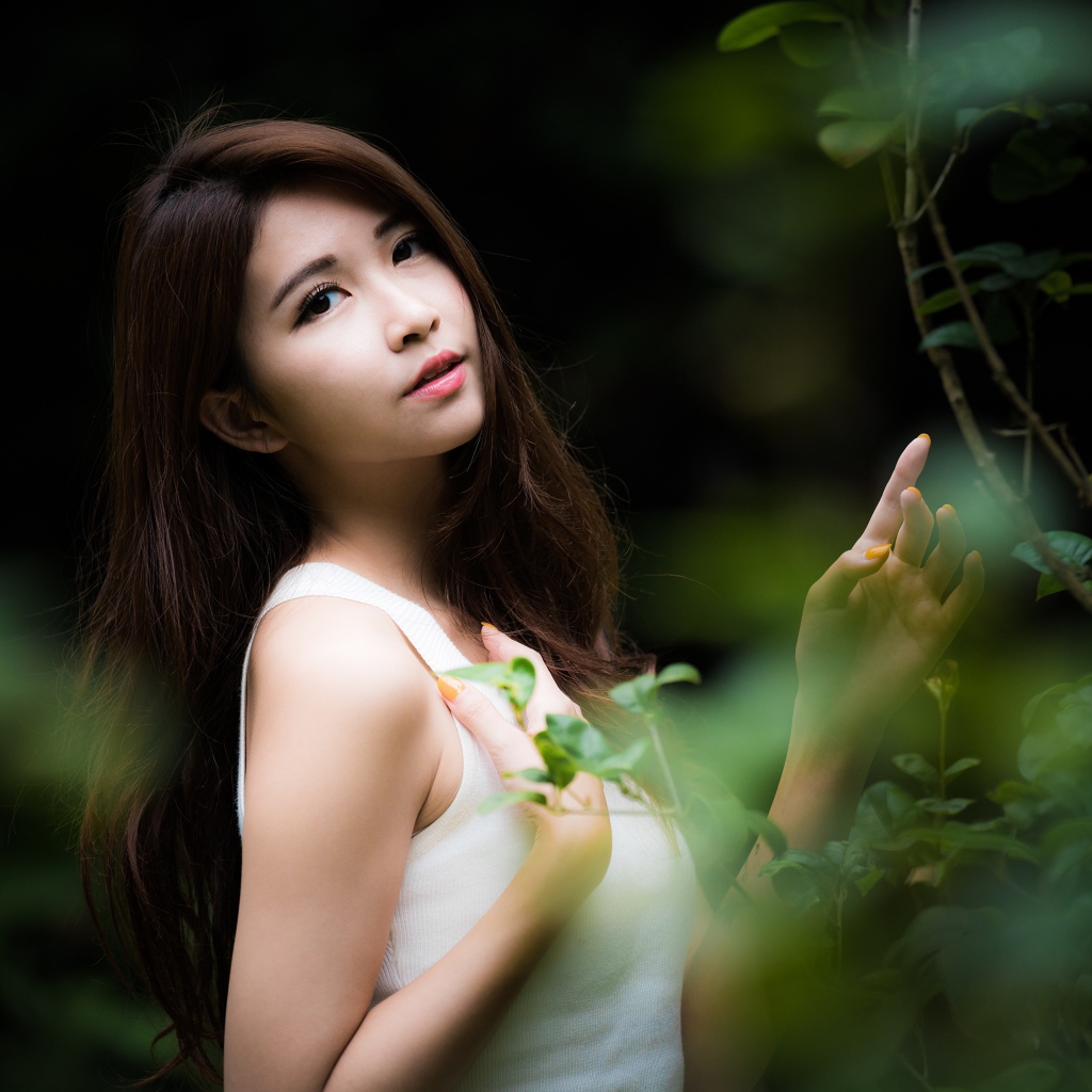 Милая азиатка в белом стоит у зеленых листьев