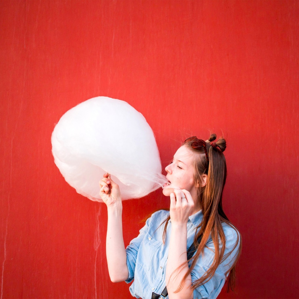 Девушка ест сладкую вату на красном фоне 