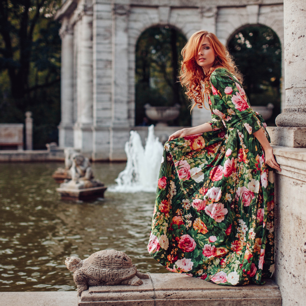 Девушка в красивом цветастом платье у пруда в парке 